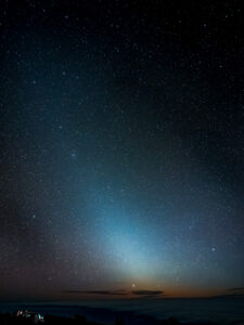 Faint cone of zodiacal light rising from the horizon, deep star field above, parked car silhouetted bottom-left, La Palma.