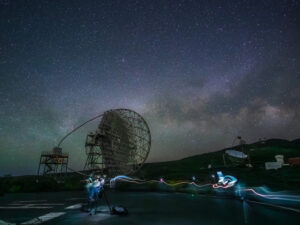 Long-exposure night scene of a MAGIC Cherenkov telescope at the Roque de los Muchachos observatory, with painted-light trails dancing across the foreground, La Palma.
