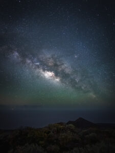 The Milky Way's galactic core hanging above a volcanic mountain ridge with subtle green airglow on the horizon, La Palma.