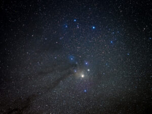 Deep-sky photograph of the Rho Ophiuchi cloud complex around the bright red star Antares, with dark nebulae winding against rich star fields.