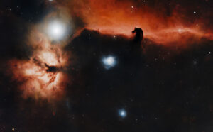 Deep-sky telescope image of the Horsehead Nebula silhouetted against red emission gas, with the bright Flame Nebula adjacent, in Orion.