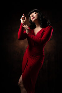 Colour fashion portrait of Helen in a floor-length red dress with a thigh slit, classic Hollywood pose, dark studio backdrop.