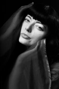 Black-and-white beauty close-up of Helen with a sheer veil-like scarf wrapped around the shoulders, soft direct gaze, atmospheric studio light.