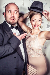 Colour photo-booth shot at the Cygnet Players 20th anniversary celebration of a man in a tuxedo pulling a comedy expression and a woman in a beige lace dress wearing his hat.
