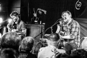Black-and-white live music photograph of Elbow performing an acoustic set at Banquet Records Pryzm, Kingston, a packed crowd close to the stage.