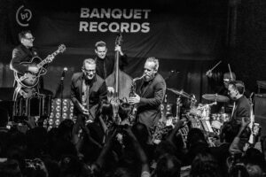 Black-and-white live music photograph of Jeff Goldblum and his band performing at Banquet Records Pryzm, Kingston — saxophone, double bass and guitar on stage.