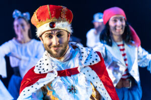 Theatrical performance photograph of a young actor dressed as a king in red and white robes with crown and royal jewels, from the PLOS production of Dick Whittington.