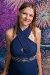Photo-booth portrait of a young woman in a navy halter dress with a jewelled belt at the Cygnet Players 25th anniversary, fireworks backdrop.