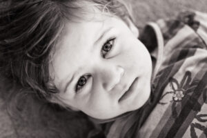 Black-and-white close-up of a young child with curly hair, looking up at the camera with a thoughtful soft gaze.