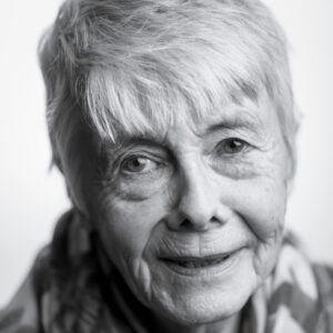 Black-and-white close-up portrait of an elderly woman with short white hair, a gentle smile and a deeply lined face, soft natural light.