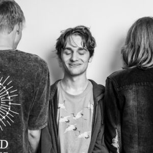 Black-and-white group portrait of school friends, the central figure smiling with eyes closed, the other two flanking him with their backs to camera.