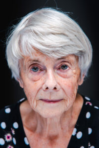 Black-and-white close-up portrait of an older woman with short white hair, bright eyes, freckles and a polka-dot top.