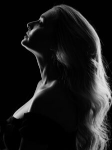 Black-and-white profile portrait of a woman with long wavy blonde hair, head tilted upward, sculpted light defining her neck and shoulders.