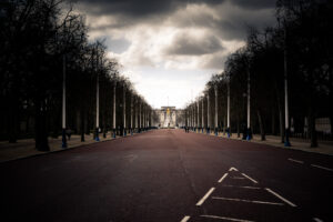 Long-exposure photograph looking down The Mall toward Buckingham Palace under dramatic clouds, the avenue eerily empty of traffic.