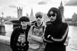 Black-and-white candid of three young men with face coverings or eye-strips standing on Westminster Bridge with the Houses of Parliament and scaffolded Big Ben behind.