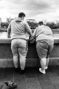 Black-and-white candid of two men leaning over the South Bank embankment wall looking across the Thames, a pigeon in the foreground.