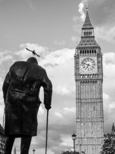 Black-and-white photograph of the Winston Churchill statue in Parliament Square with Big Ben behind, a bird flying over Churchill's head.