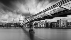 Long-exposure black-and-white photograph of the Millennium Bridge stretching across the Thames toward St Paul's Cathedral, smoothed water and streaked clouds.